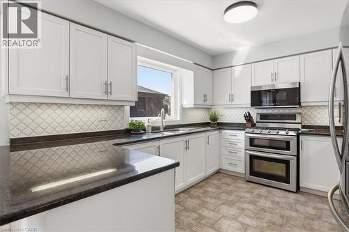 Kitchen featuring white cabinetry with brushed nickel hardware, dark countertops, and a decorative tile backsplash - 19 Forestview Drive, Cambridge, ON - Indoor Photo Showing Kitchen
