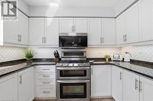 Modern kitchen featuring white cabinetry, dark countertops, a stainless steel range with double ovens, a built-in microwave, and a decorative tiled backsplash - 19 Forestview Drive, Cambridge, ON - Indoor Photo Showing Kitchen