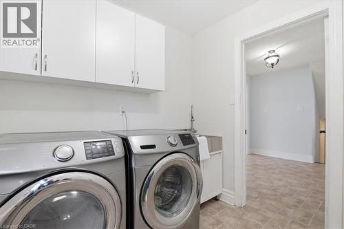 Dedicated laundry area featuring white upper cabinetry with curved hardware, a utility sink with a high-arc faucet, and tiled flooring - 19 Forestview Drive, Cambridge, ON - Indoor Photo Showing Laundry Room