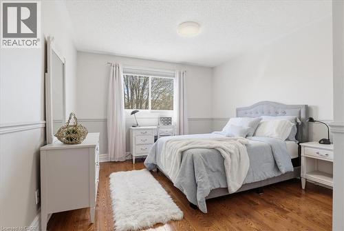Bright bedroom featuring hardwood flooring, a large window, white walls, two-tone wainscoting, and a ceiling-mounted light fixture - 19 Forestview Drive, Cambridge, ON - Indoor Photo Showing Bedroom