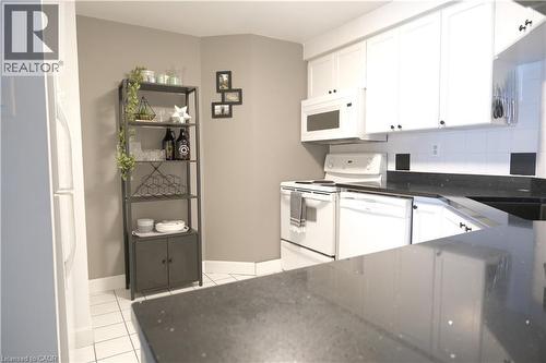 Kitchen featuring white cabinetry, black countertops, white subway tile backsplash, and white appliances including a range, microwave, and dishwasher - 175 Hunter Street E Unit# 301, Hamilton, ON - Indoor Photo Showing Kitchen