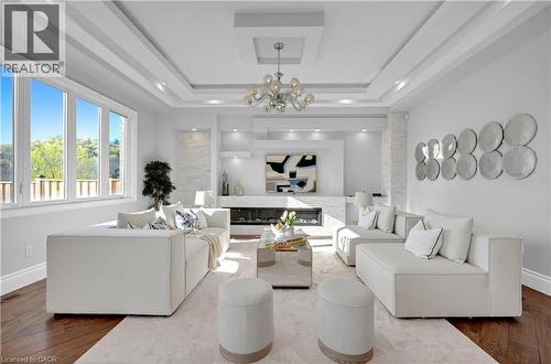 Spacious living area featuring expansive windows, wood-finish flooring, a contemporary fireplace with stone surround, recessed lighting, and a multi-tiered tray ceiling with a chandelier - 7 Riesling Court, Hamilton, ON - Indoor Photo Showing Living Room