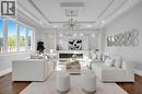 Spacious living area featuring expansive windows, wood-finish flooring, a contemporary fireplace with stone surround, recessed lighting, and a multi-tiered tray ceiling with a chandelier - 7 Riesling Court, Hamilton, ON  - Indoor Photo Showing Living Room 