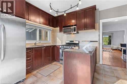 Kitchen featuring dark wood-finish cabinetry, stainless steel appliances, a gas range, a track lighting fixture, and a peninsula with a stone countertop - 204 Beach Boulevard, Hamilton, ON - Indoor Photo Showing Kitchen