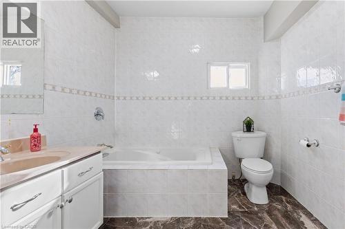 Bathroom featuring a built-in tub, white tiled walls with a decorative border, and a vanity with a light-colored countertop - 204 Beach Boulevard, Hamilton, ON - Indoor Photo Showing Bathroom