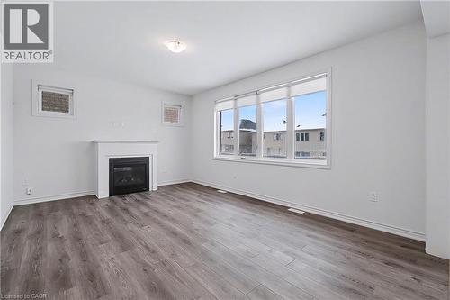 Spacious living area featuring wood-finish flooring, a contemporary fireplace with a white mantel, and a multi-pane window - 123 Rea Drive, Fergus, ON - Indoor Photo Showing Other Room With Fireplace