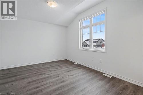 Vaulted ceiling room featuring a large multi-pane window, wood-finish flooring, white baseboards, and a flush-mount ceiling light - 123 Rea Drive, Fergus, ON - Indoor Photo Showing Other Room