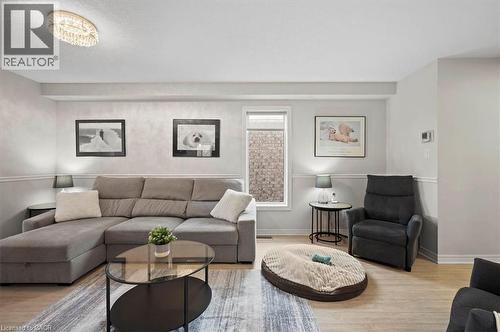 Living area featuring wood-finish flooring, a contemporary flush mount ceiling light, and a window with a stone wall visible - 30 Heatherwood Place, Kitchener, ON - Indoor Photo Showing Living Room