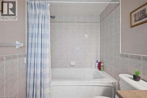 White bathtub with integrated shower, surrounded by light-toned square wall tiles and a decorative accent border - 30 Heatherwood Place, Kitchener, ON - Indoor Photo Showing Bathroom