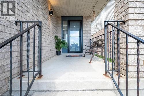 Inviting front porch featuring a dark grey storm door, complementary exterior sconce lighting, and durable brick facade accents - 30 Heatherwood Place, Kitchener, ON - Outdoor With Exterior