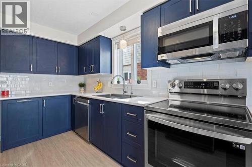 Modern kitchen featuring blue cabinetry, stainless steel appliances, a white subway tile backsplash, light countertops, and wood-finish flooring - 30 Heatherwood Place, Kitchener, ON - Indoor Photo Showing Kitchen With Upgraded Kitchen