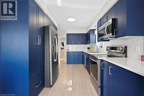 Galley kitchen featuring deep blue cabinetry, stainless steel appliances, light wood-finish flooring, white subway tile backsplash, and white countertops - 30 Heatherwood Place, Kitchener, ON - Indoor Photo Showing Kitchen With Upgraded Kitchen