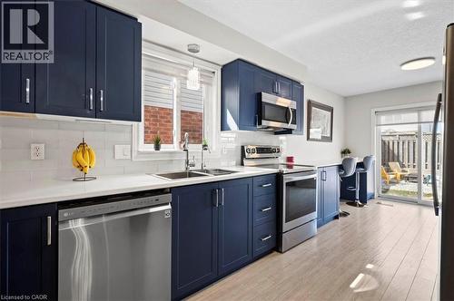 Modern kitchen featuring deep blue cabinetry, stainless steel appliances, white subway tile backsplash, and light wood-finish flooring - 30 Heatherwood Place, Kitchener, ON - Indoor Photo Showing Kitchen With Double Sink With Upgraded Kitchen
