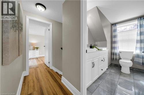 Hallway featuring wood-finish flooring, leading to a bathroom with a white vanity, a toilet, and a window with blinds - 26 Peachtree Crescent, Cambridge, ON - Indoor Photo Showing Bathroom