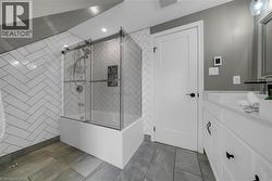 Contemporary bathroom featuring a bathtub with a sliding glass enclosure, herringbone pattern wall tile, and recessed lighting - 