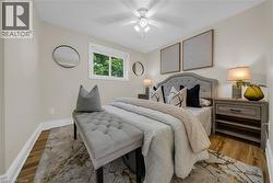 Bedroom featuring neutral wall tones, wood-finish flooring, a white window frame, and a ceiling fan with integrated lighting - 
