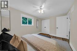 Bedroom featuring wood-finish flooring, a contemporary ceiling fan with integrated lighting, a double-panel closet with matte black hardware, and a single window with white trim - 