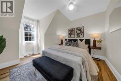 Bedroom featuring a vaulted ceiling with a flush-mount light fixture, wood-finish flooring, a window with white trim, and light-toned walls - 