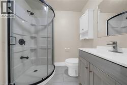 Bathroom featuring a curved glass shower enclosure with black trim, a gray wood-finish vanity with a white countertop, and a coordinating wall-mounted storage cabinet - 