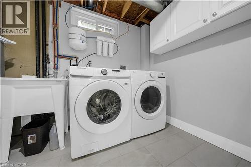 Dedicated laundry area featuring a utility sink, two laundry machines, overhead white cabinetry, and gray tile flooring - 26 Peachtree Crescent, Cambridge, ON - Indoor Photo Showing Laundry Room