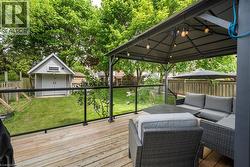 Wood-finish deck featuring a glass railing and a permanent gazebo with integrated string lighting - 