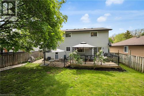 Expansive backyard featuring a manicured lawn, a raised wood-finish deck with glass panel railing, and a ground-level paver patio - 26 Peachtree Crescent, Cambridge, ON - Outdoor With Deck Patio Veranda
