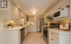 Kitchen featuring ample cream-colored cabinetry, stainless steel appliances, light-toned countertops, tile flooring. Photo Virtually Staged. - 