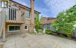 Expansive brick exterior featuring a wooden elevated deck, ground-level patio, and surrounding garden beds with mature shrubs - 