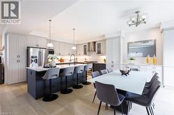 Open-concept kitchen featuring an oversized island with seating, pendant lighting, stainless steel appliances, and light wood-finish flooring - 