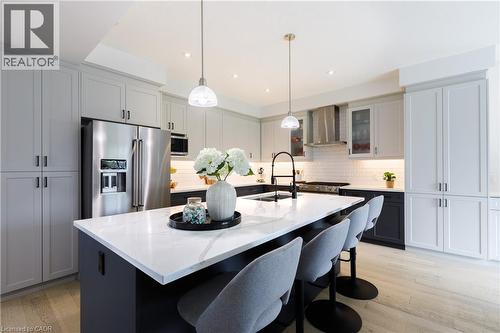 Modern kitchen featuring a large island with a substantial white countertop, light gray upper cabinetry, two-tone lower cabinetry, stainless steel appliances, and wood-finish flooring - 581 Doonwoods Crescent, Kitchener, ON - Indoor Photo Showing Kitchen With Stainless Steel Kitchen With Upgraded Kitchen
