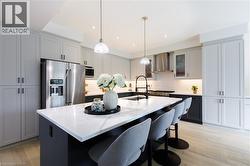 Modern kitchen featuring a large island with a substantial white countertop, light gray upper cabinetry, two-tone lower cabinetry, stainless steel appliances, and wood-finish flooring - 