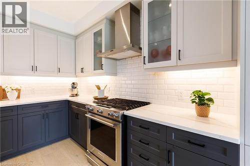 Contemporary kitchen featuring two-tone cabinetry, a stainless steel gas range with a matching range hood, white subway tile backsplash, white countertops, and under-cabinet lighting - 581 Doonwoods Crescent, Kitchener, ON - Indoor Photo Showing Kitchen With Upgraded Kitchen