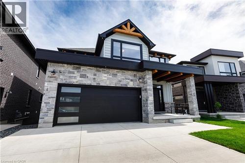 Contemporary residence featuring stone and siding exterior, a prominent black garage door with horizontal windows, a covered front entry with stone columns, and a concrete driveway - 581 Doonwoods Crescent, Kitchener, ON - Outdoor With Facade