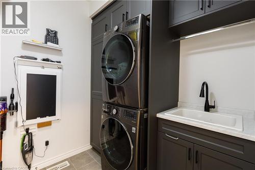 Laundry area featuring stacked appliances, dark cabinetry, and a utility sink with a black faucet - 581 Doonwoods Crescent, Kitchener, ON - Indoor Photo Showing Laundry Room