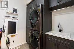 Laundry area featuring stacked appliances, dark cabinetry, and a utility sink with a black faucet - 