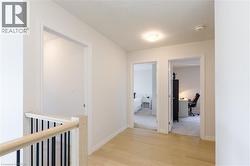 Second-story hallway featuring light wood-finish flooring, white walls, white trim, and a contemporary flush-mount ceiling light - 