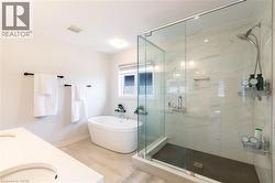 Spacious bathroom featuring a frameless glass shower enclosure with tile surround, a freestanding soaking tub, and a vanity with an integrated sink - 