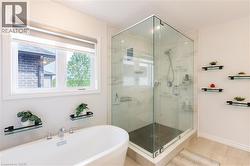 Contemporary bathroom featuring a freestanding soaking tub with deck-mounted chrome fixtures, a corner glass-enclosed shower with stone-look tile surround, and light-toned floor tile - 