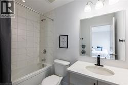 Bathroom with a white tiled shower and tub combination, a toilet, and a vanity featuring a matte black faucet and an oval undermount sink set into a light-toned countertop - 