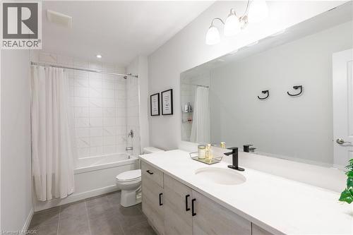 Bathroom featuring a white bathtub and shower with tile surround, a single vanity with an integrated sink, a large wall-mounted mirror, and gray tile flooring - 581 Doonwoods Crescent, Kitchener, ON - Indoor Photo Showing Bathroom