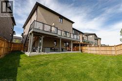 Rear exterior featuring a brick facade, a raised deck with glass panel railings and exterior stairs, a covered lower patio, and a spacious lawn enclosed by wood fencing - 