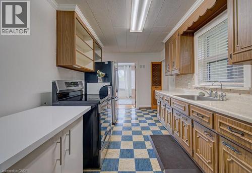 Galley kitchen featuring wood-finish cabinetry, a stainless steel sink, and a black electric range - 128 Pollock Avenue, Cambridge, ON - Indoor Photo Showing Kitchen
