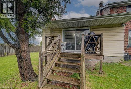 Rear exterior featuring a wooden deck with railing, sliding glass door, and a mature tree - 128 Pollock Avenue, Cambridge, ON - Outdoor