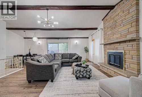 Living area featuring wood-finish flooring, exposed ceiling beams, and a stone-clad fireplace with hearth and mantel - 128 Pollock Avenue, Cambridge, ON - Indoor Photo Showing Living Room With Fireplace