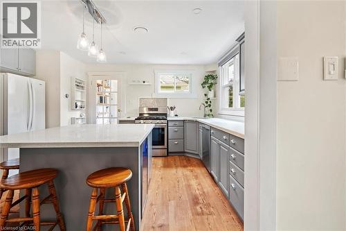 Kitchen featuring a central island with countertop seating, wood-finish flooring, light grey cabinetry, stainless steel range, and a tiled backsplash - 6295 Guelph Line, Burlington, ON - Indoor Photo Showing Kitchen With Upgraded Kitchen