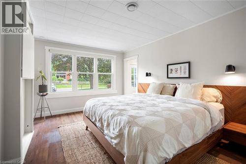 Hardwood flooring throughout featuring a large window, a wood-paneled accent wall, and built-in wall sconces - 6295 Guelph Line, Burlington, ON - Indoor Photo Showing Bedroom