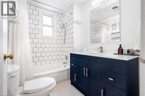 Bathroom featuring a dark blue vanity with silver hardware, a white countertop, a rectangular mirror, and subway tile surrounding the tub - 6295 Guelph Line, Burlington, ON - Indoor Photo Showing Bathroom
