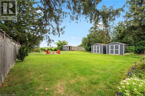 Expansive green lawn featuring two dark-toned storage sheds with white trim, a smaller light-toned shed with a red door, and a wooden perimeter fence - 6295 Guelph Line, Burlington, ON - Outdoor