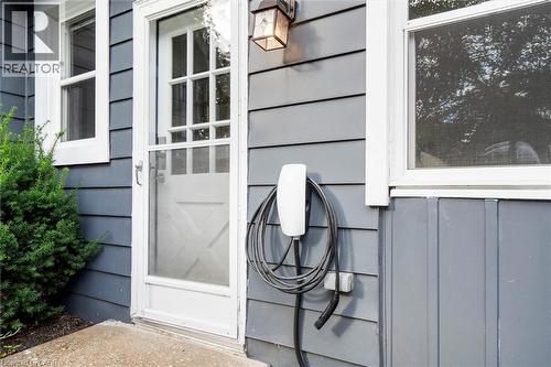 Exterior featuring horizontal siding, white trim, a front entry door with storm door, a wall-mounted light fixture, and an electric vehicle charging station - 6295 Guelph Line, Burlington, ON - Outdoor With Exterior