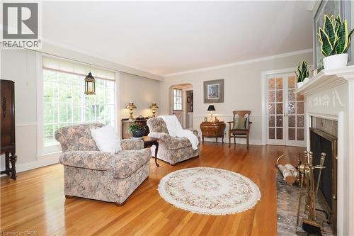 Hardwood flooring throughout featuring a decorative fireplace with a stone surround, a large window providing ample natural light, white crown molding, and double French doors with textured glass pane - 2023 Coronation Boulevard, Cambridge, ON - Indoor Photo Showing Living Room